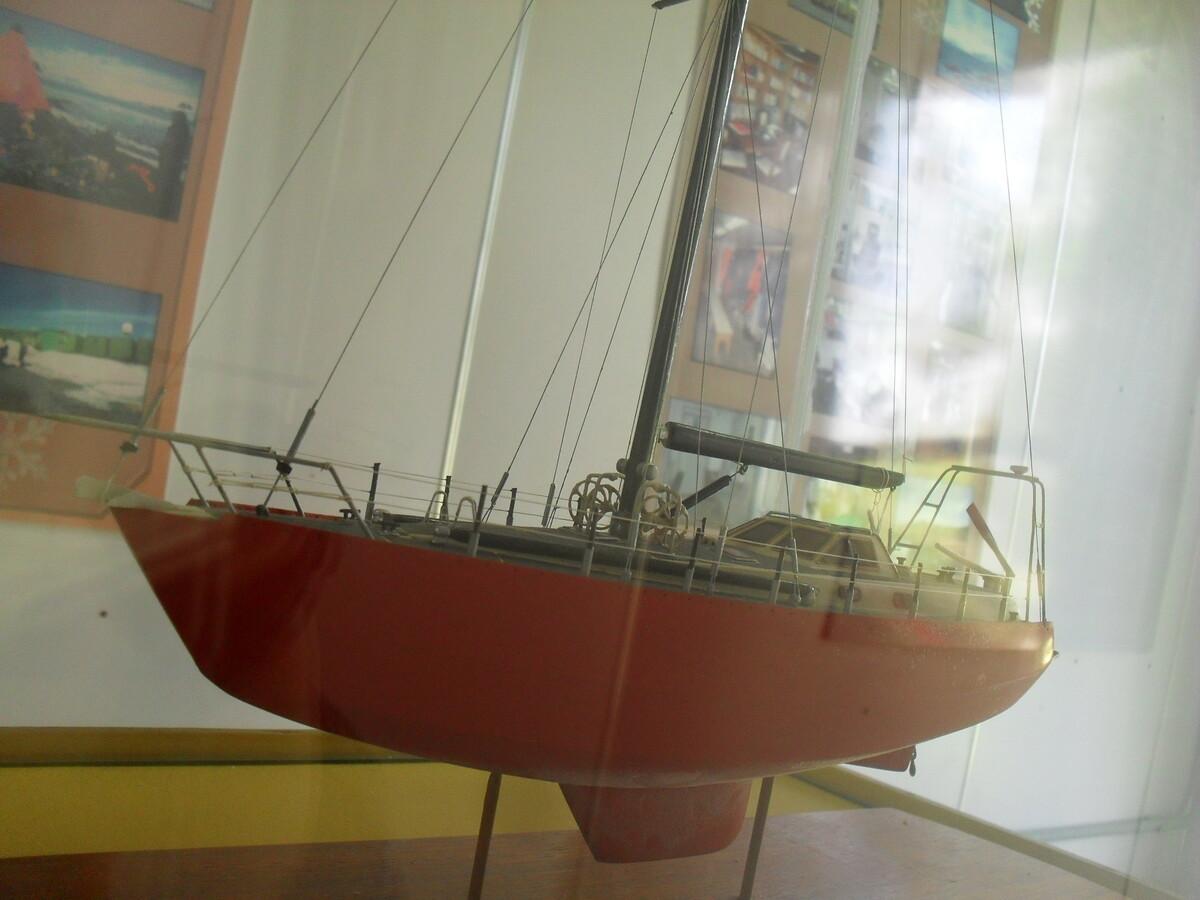 Foto de uma maquete de um barco vermelho exposto em um museu, com reflexos no vidro que o protege.